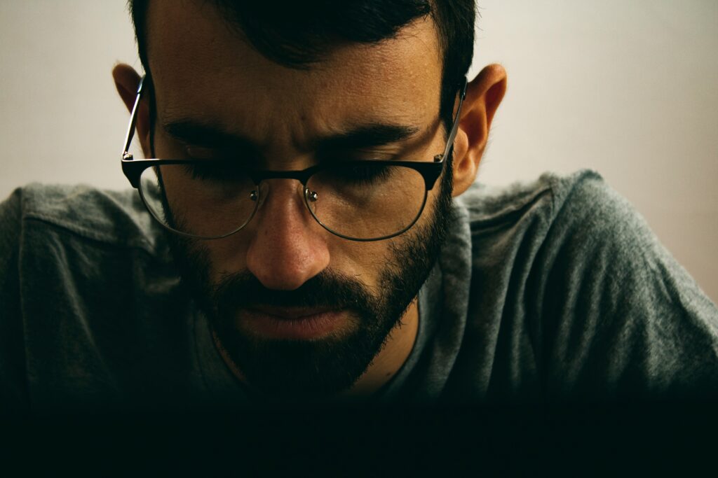 A close-up of a man with glasses looking downward, showing emotional heaviness and internal struggle.