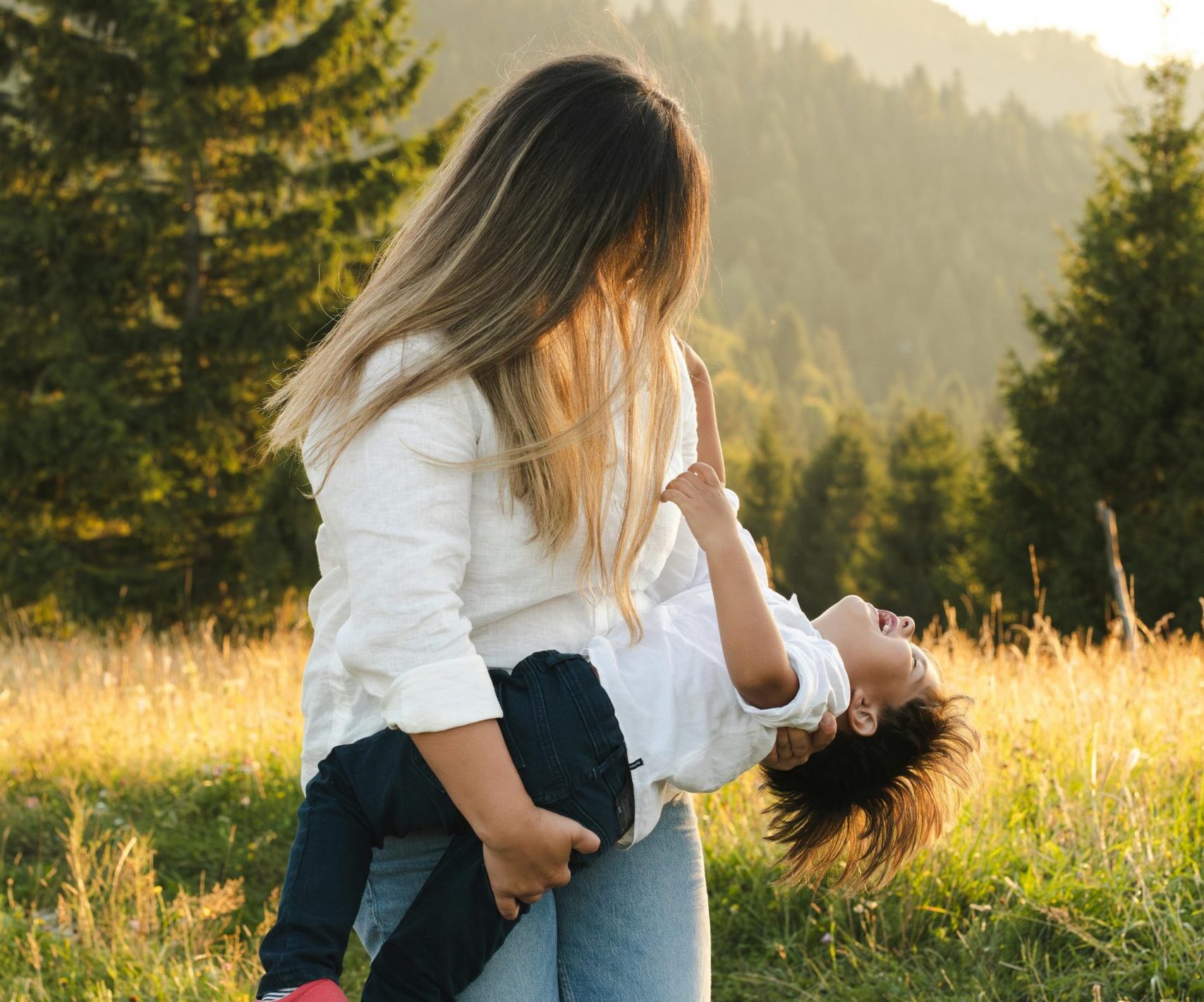 Mother and daughter embrace on a grass field.