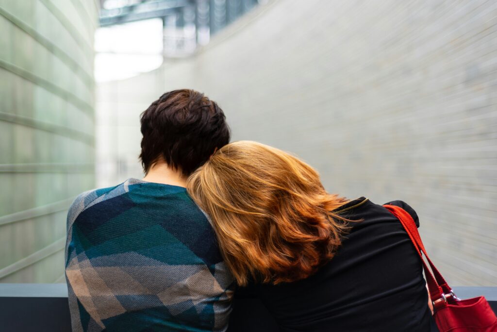 Two people sitting closely, one resting their head on the other's shoulder for comfort.