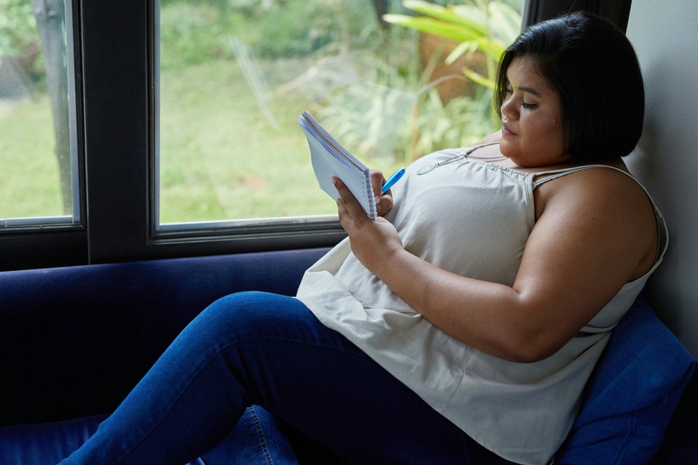 A woman writing in a notebook by the window, symbolizing emotional awareness and personal growth through therapy.