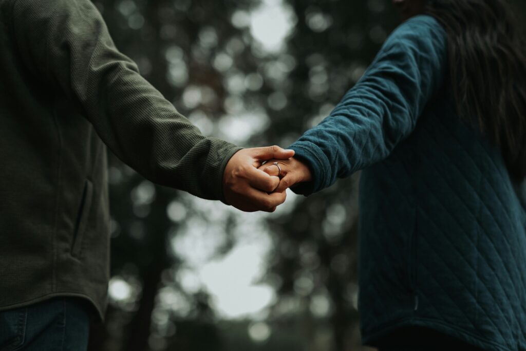 A couple holding hands together in the woods.