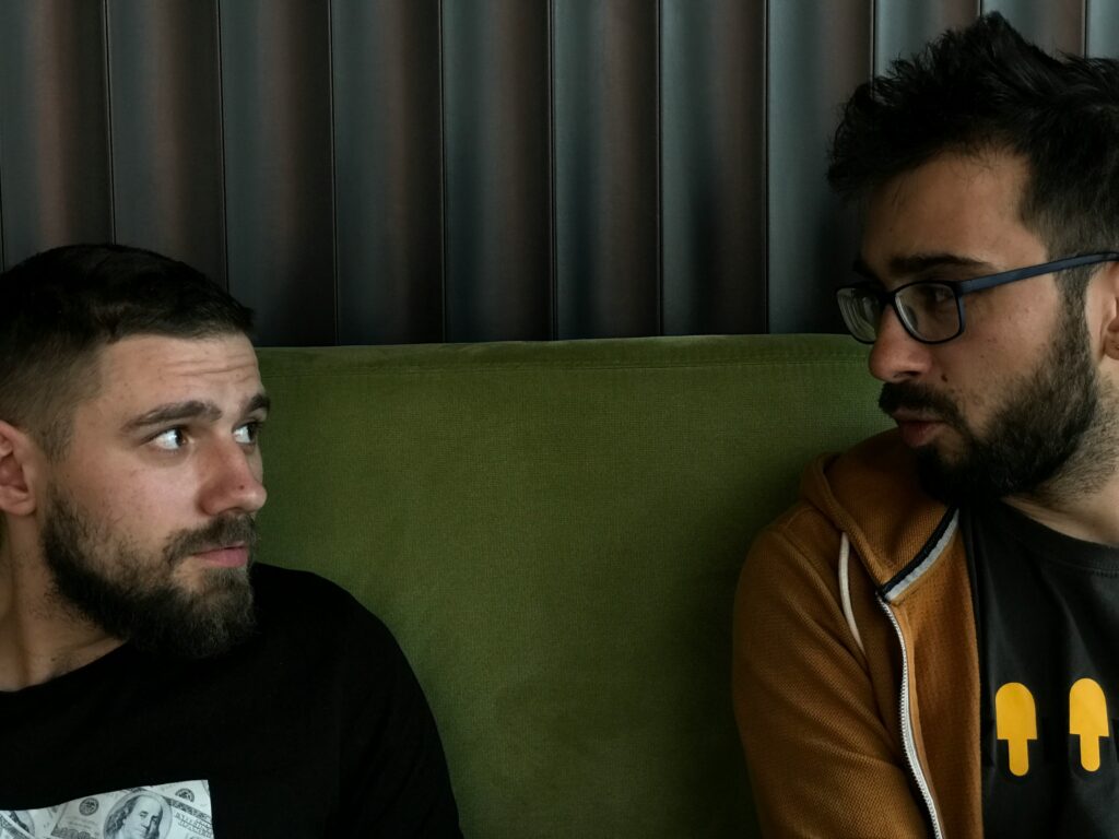 Two men making eye contact on a couch, engaged in serious emotional dialogue.