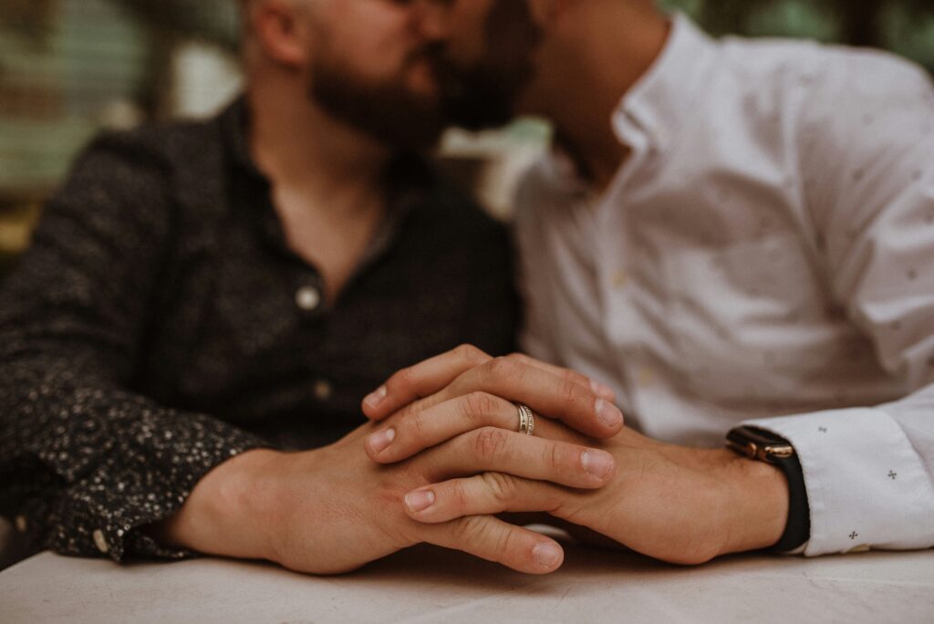 A close-up of a couple’s hands intertwined while they kiss, symbolizing emotional trust and intimacy.