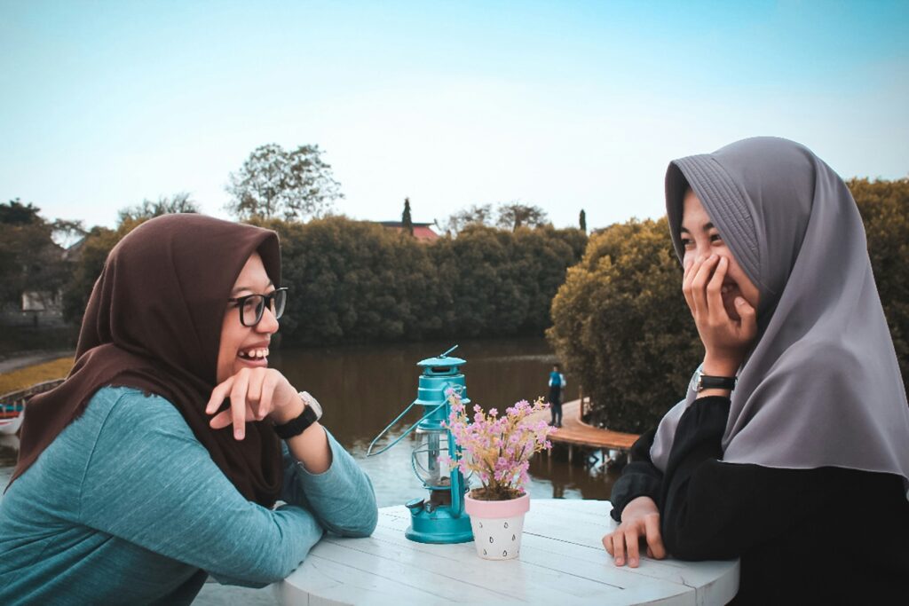 Two women at a cafe laughing warmly, symbolizing emotional openness.